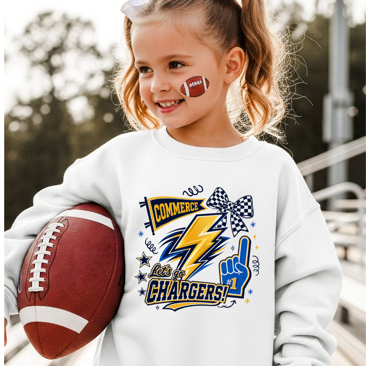 Child wearing a white sweatshirt with 'Commerce Chargers' design, holding a football.