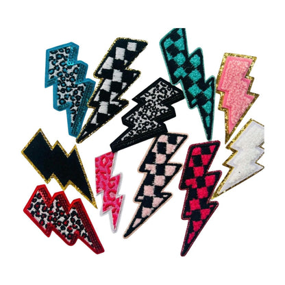 May include: A collection of 12 lightning bolt shaped iron on patches in various colors and patterns including pink, black, white, blue, and red. The patches have checkered, leopard print, and fuzzy textures.