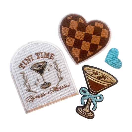 May include: Four embroidered iron-on patches. One patch is a white rectangle with brown embroidery of a martini glass with the text &#39;TINI TIME Espresso Martini&#39;. Another patch is a brown and tan checkered heart. The third patch is a blue heart. The fourth patch is a brown martini glass with a blue bow and a brown swirl design.