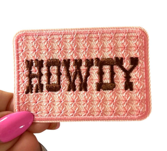 May include: A pink embroidered patch with the word 'HOWDY' in brown thread.