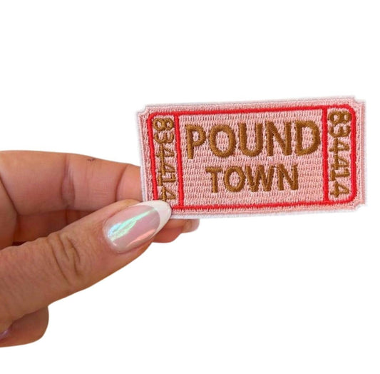 May include: A pink ticket-shaped patch with red borders and white stitching. The patch has the text &#39;POUND TOWN&#39; in brown embroidery.