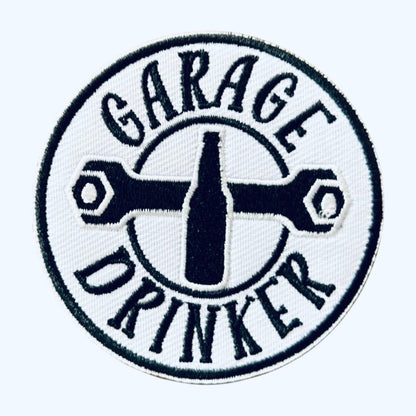 May include: A white circular patch with black embroidered text and a wrench design. The text reads &#39;Garage Drinker&#39; with a bottle shape in the center.