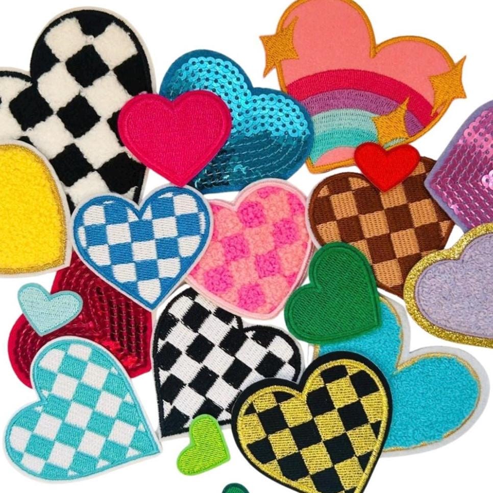 May include: A collection of colorful heart-shaped patches with various designs, including checkered, sequined, and fuzzy textures. The patches are arranged in a loose, overlapping pattern, creating a visually appealing and playful composition.