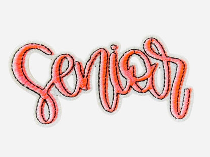 May include: A pink embroidered patch with the word &#39;Senior&#39; in a cursive font.