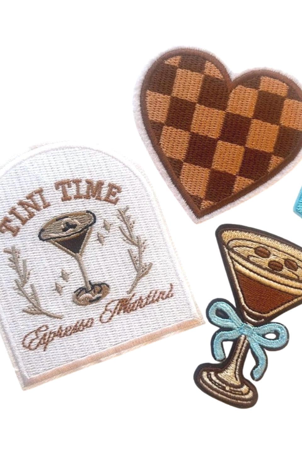May include: Four embroidered iron-on patches. One patch is a white rectangle with brown embroidery of a martini glass with the text &#39;TINI TIME Espresso Martini&#39;. Another patch is a brown and tan checkered heart. The third patch is a blue heart. The fourth patch is a brown martini glass with a blue bow and a brown swirl design.